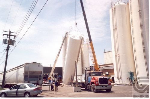 Un camion est soulevé par une grue devant des silos