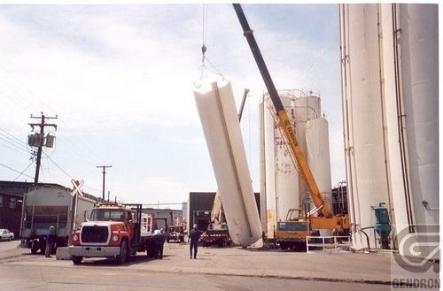 Un camion est soulevé par une grue devant des silos