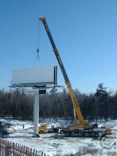 Une grande grue soulève un panneau publicitaire dans la neige