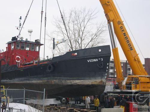 Une grande grue jaune soulève un bateau portant le nom de verma