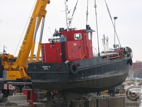 Une grande grue jaune soulève un grand bateau rouge