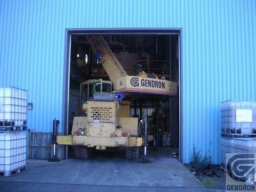 Une grue jaune est garée devant un bâtiment bleu