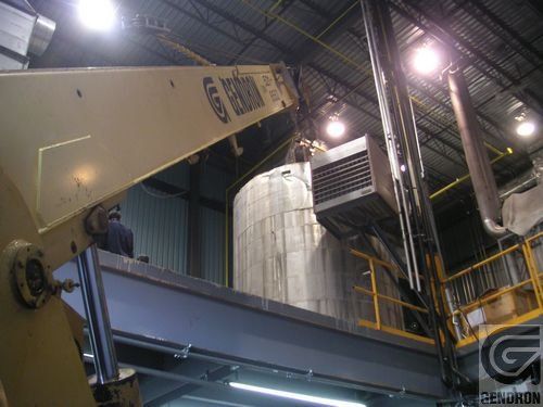 Une grue soulève un grand réservoir dans une usine.