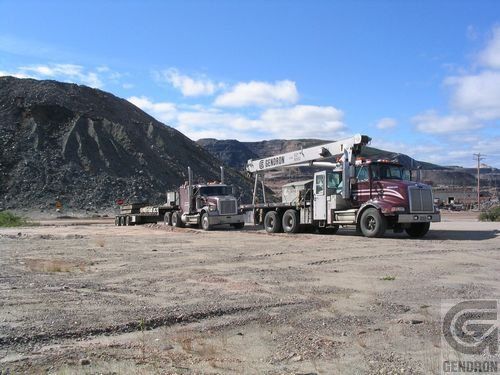 Two semi trucks are parked in a dirt field with mountains in the background