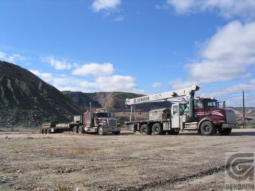 Two semi trucks are parked in a dirt field with mountains in the background