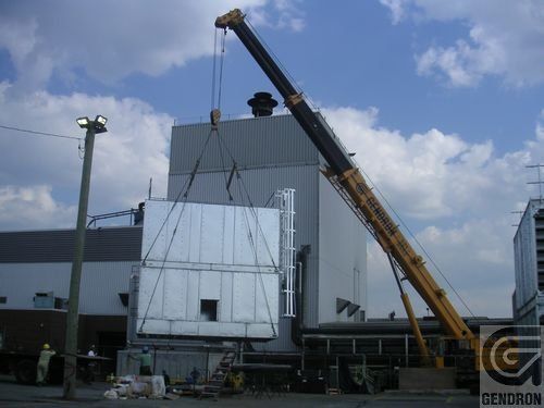 Une grande grue jaune soulève un gros morceau de métal
