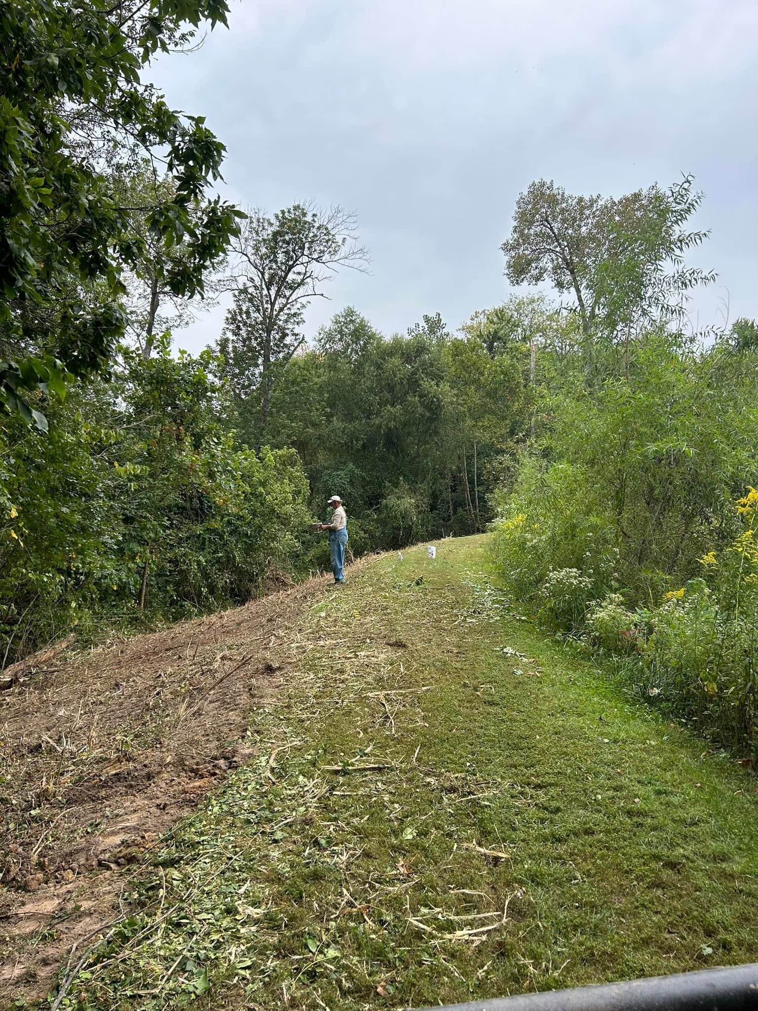 A man is mowing a lush green field with trees in the background.