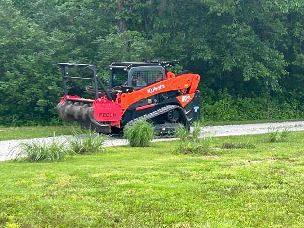 A red and black tractor is driving down a road in a field.