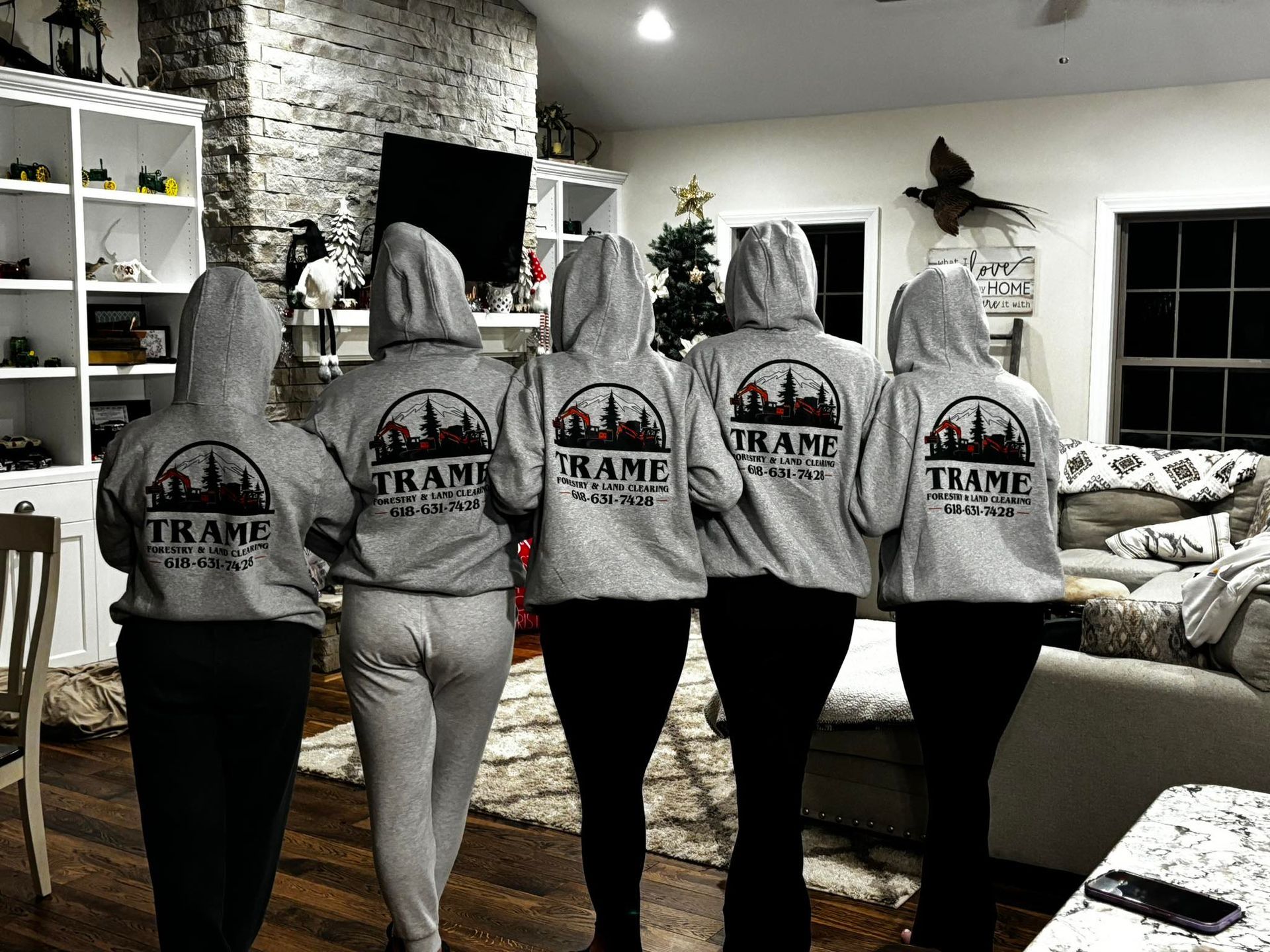 A group of women are standing in a living room wearing matching hoodies.