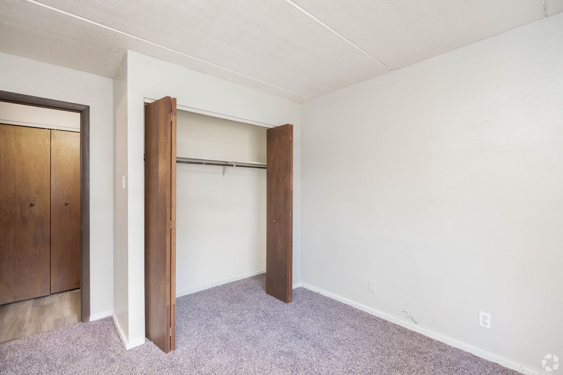 Empty room with open closet and closed wooden door. Purple carpet, white walls.