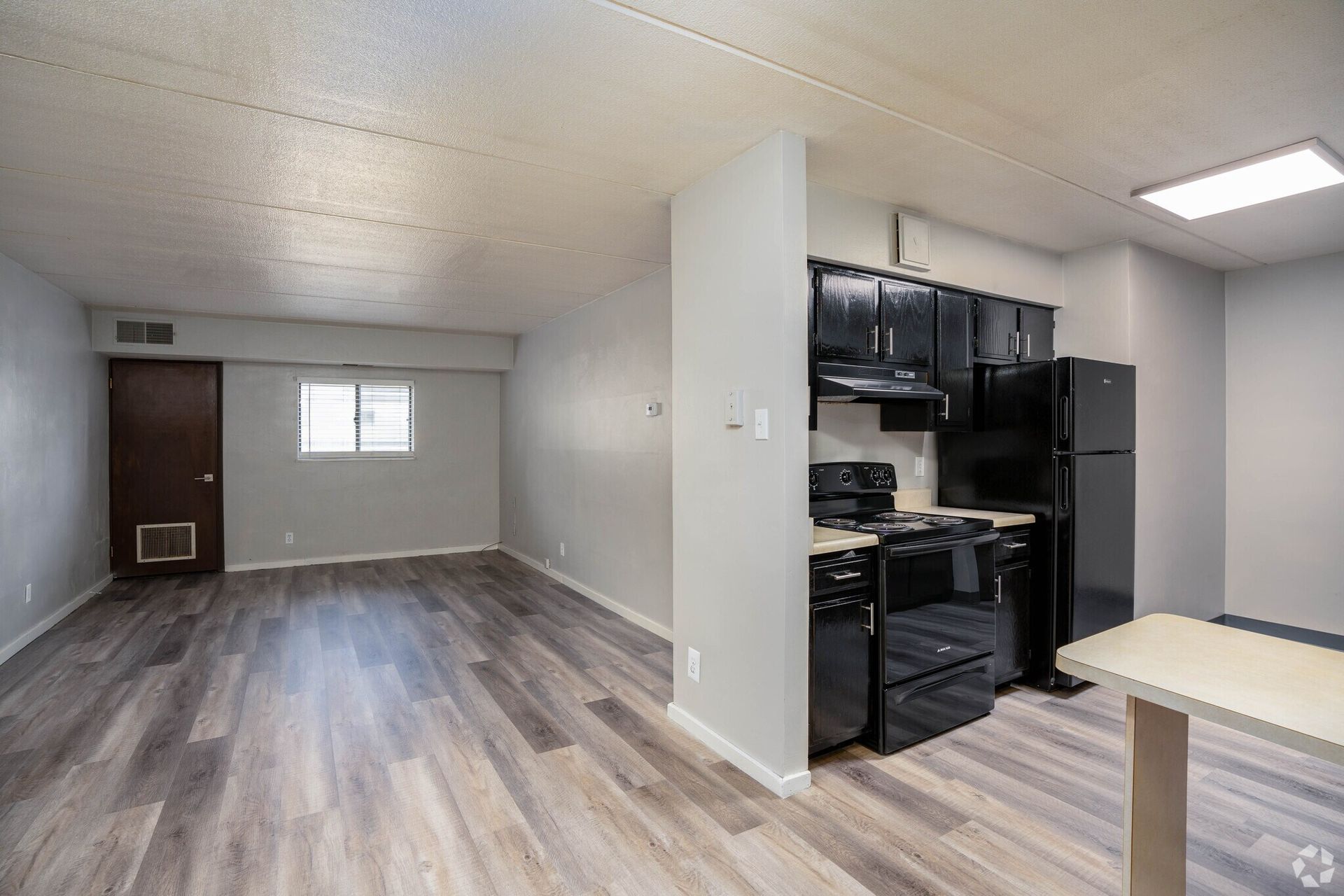 Interior of an apartment with wood-look flooring, black kitchen appliances, and gray walls.