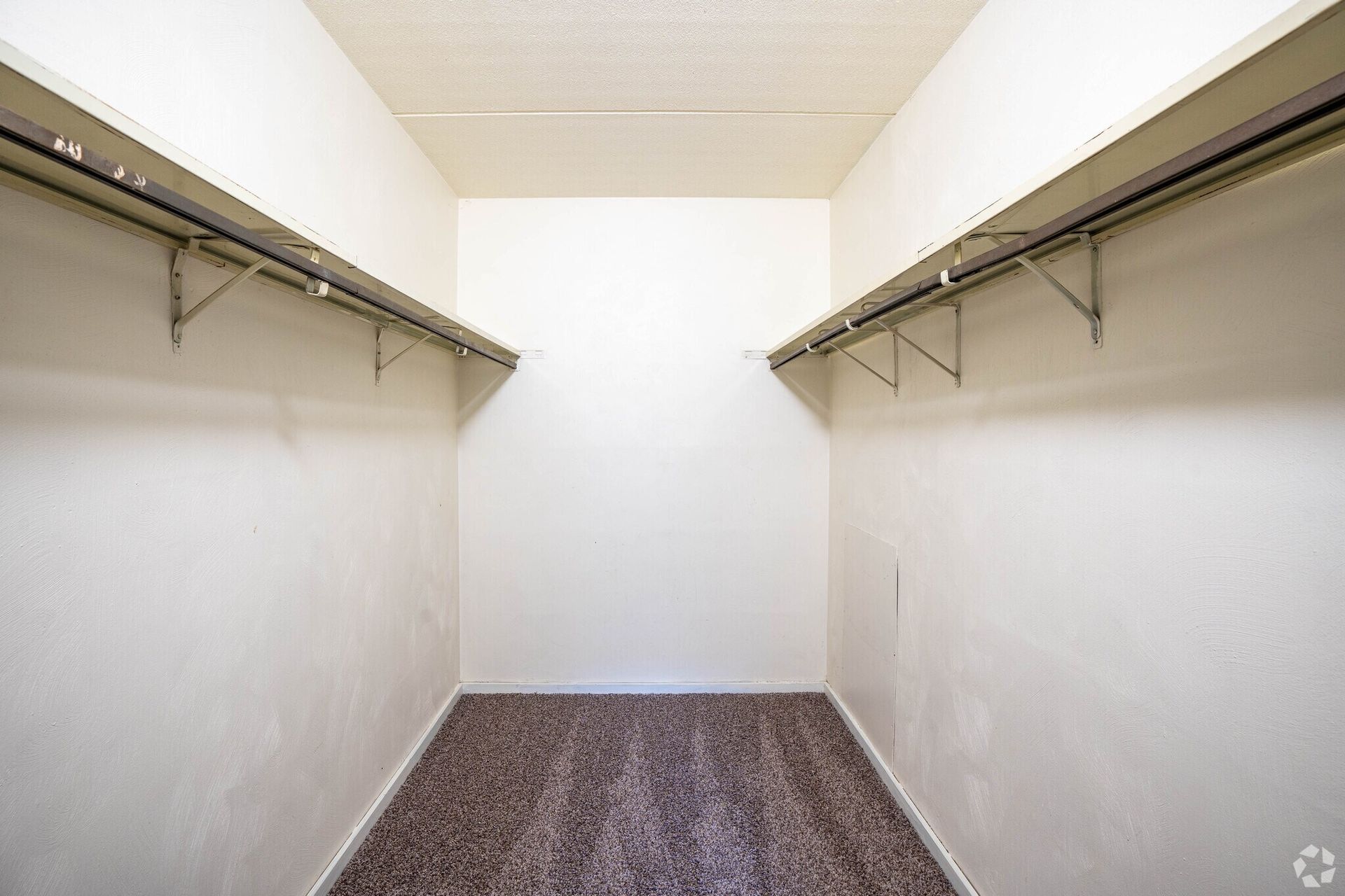 Empty walk-in closet with shelves and a carpeted floor. White walls and ceiling.