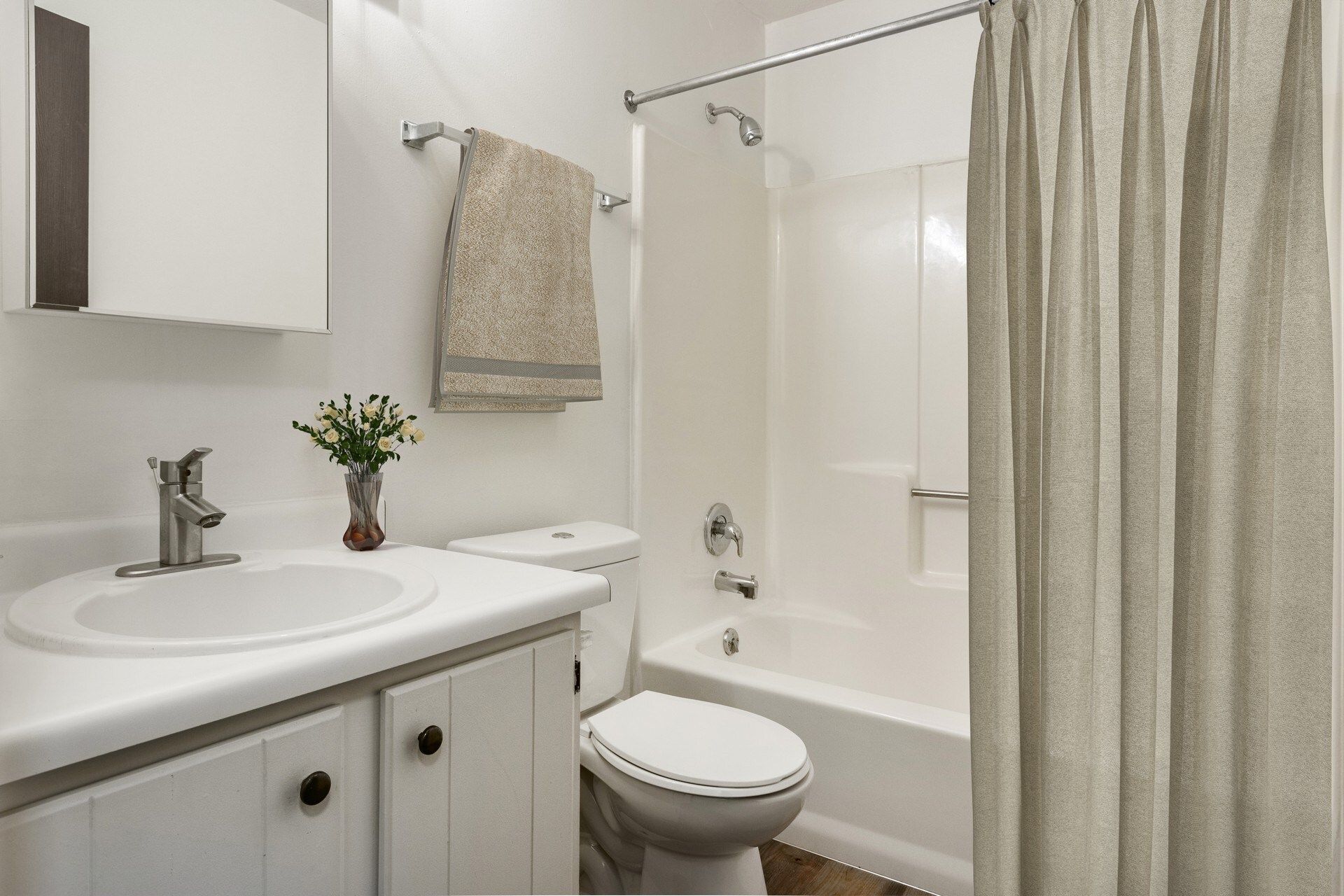 Bathroom with white sink, toilet, and shower/tub. Beige shower curtain and towel.