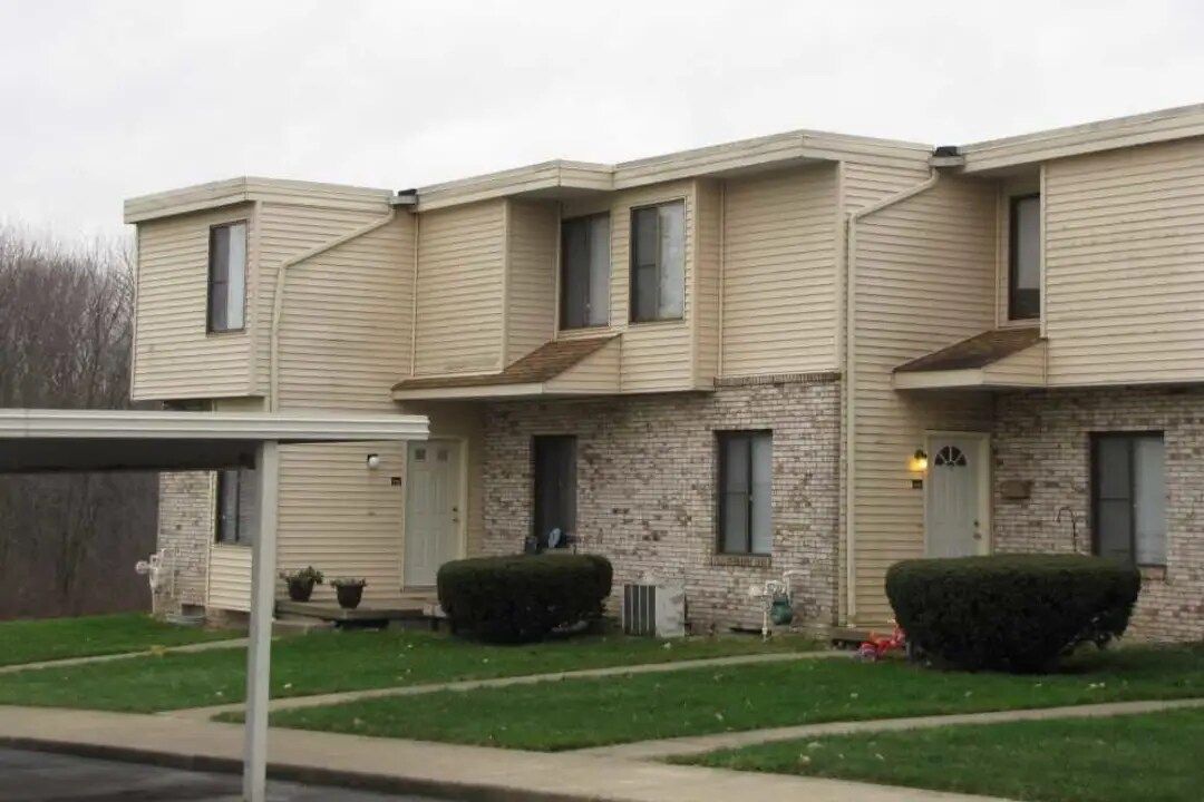 Townhouses with light tan siding, stone facade, and green lawns on an overcast day.