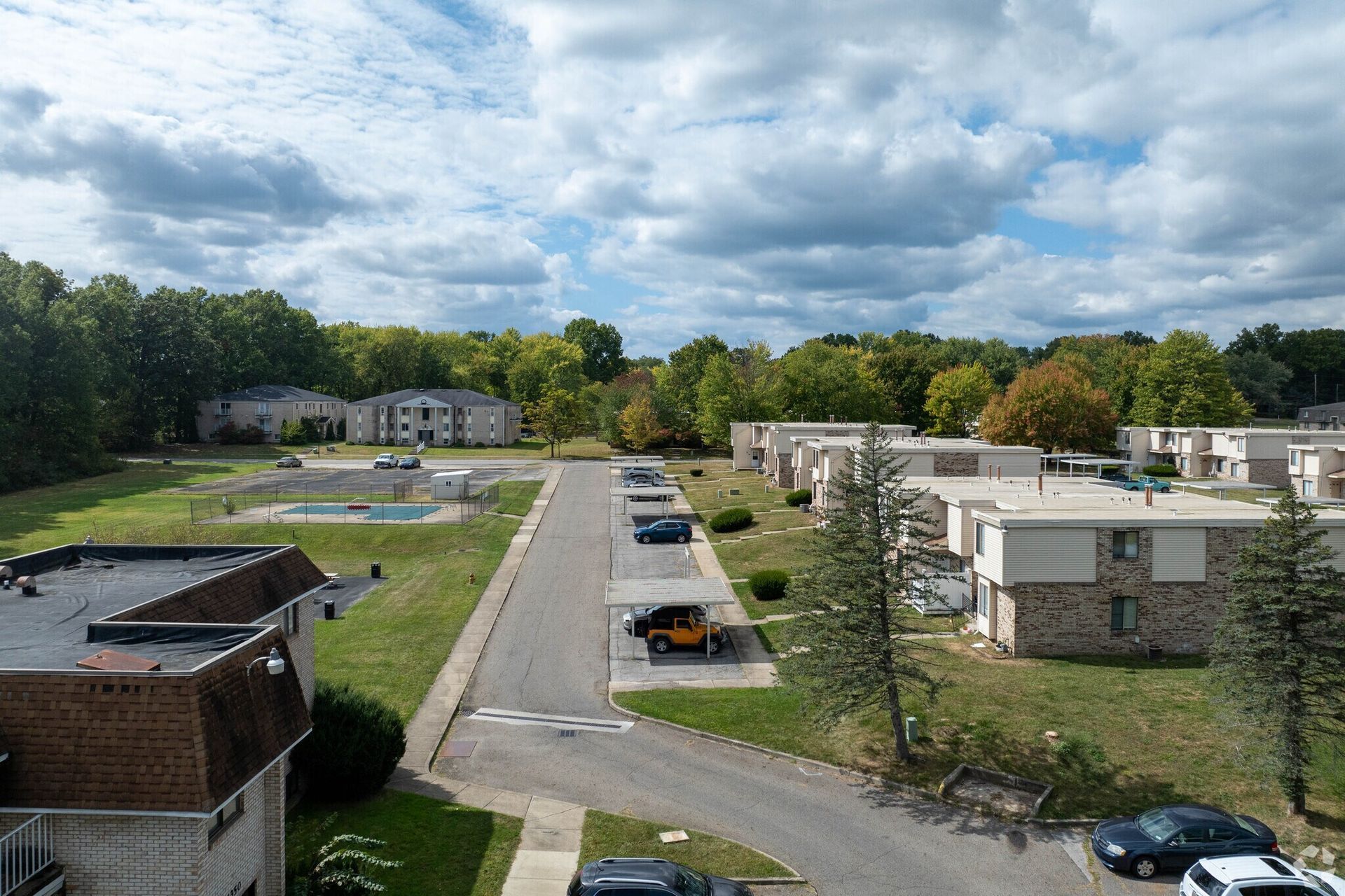Apartment complex with a street, cars, trees, and cloudy sky.