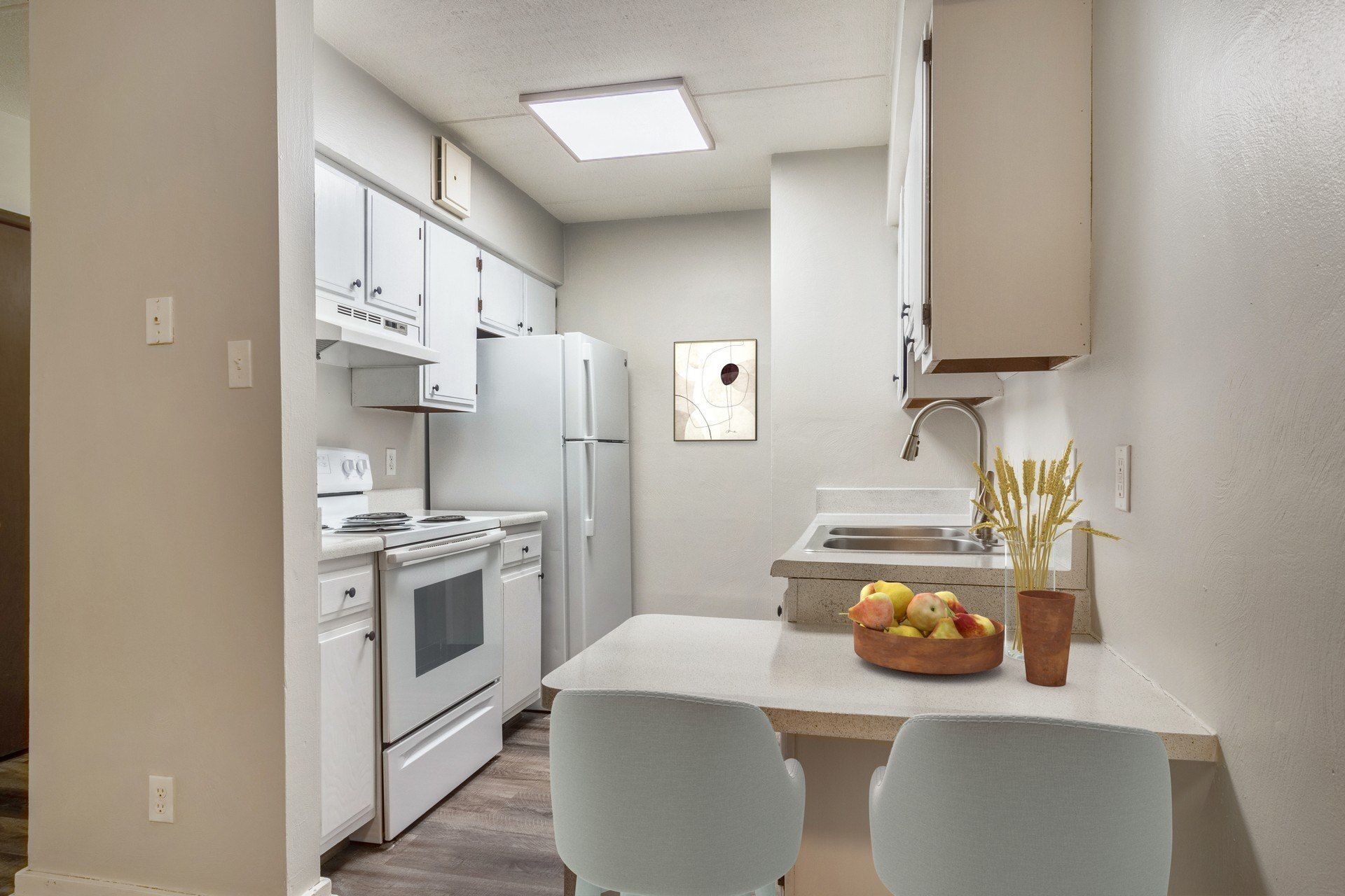 White kitchen with stove, refrigerator, cabinets, small table, two chairs, and a sink.