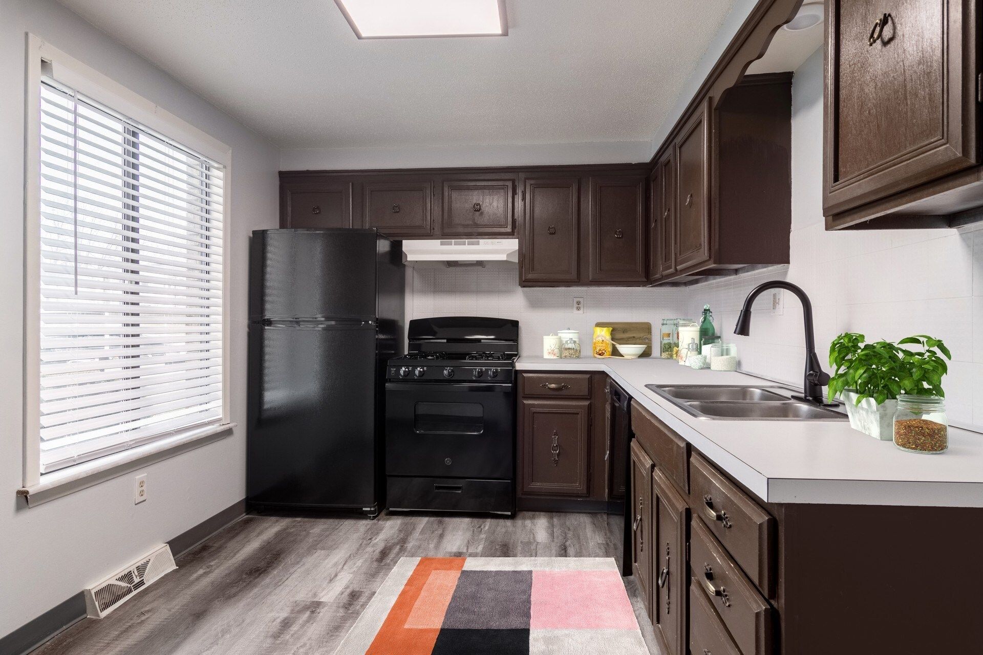 Kitchen with dark brown cabinets, black appliances, window, and gray flooring.