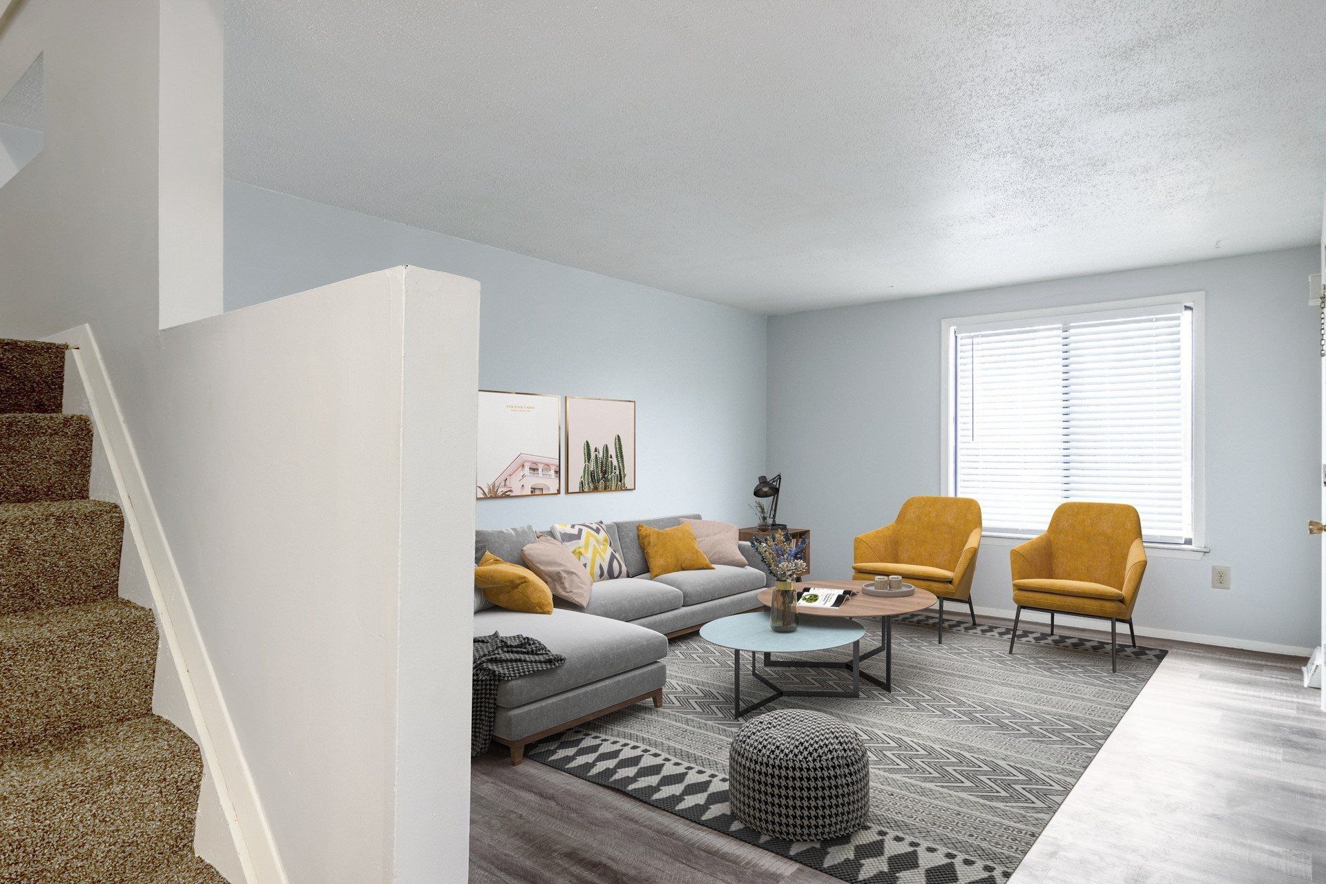 Living room with gray sofa, yellow chairs, rug, and coffee table; light blue walls, stairs.