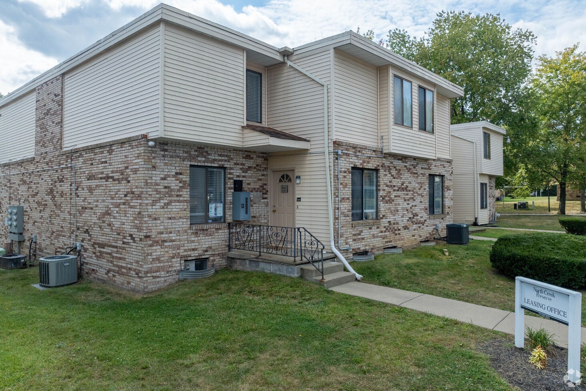 Townhouse exterior with beige siding and brick facade, green lawn and a sign.