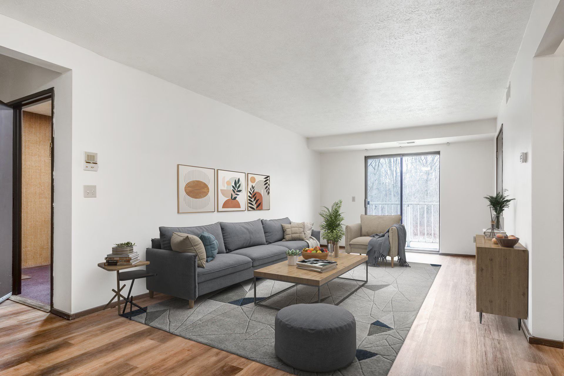 Living room with gray sofa, coffee table, rug, and sliding door to a balcony.