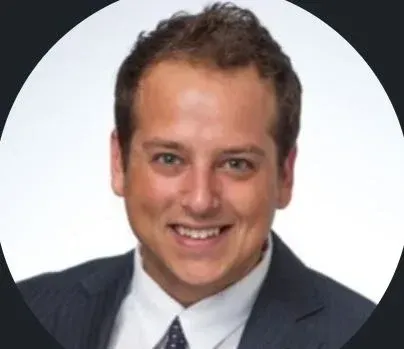 Man smiling, wearing a suit and tie, against a white background.