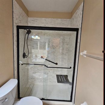 Accessible bathroom with a glass-enclosed shower featuring black fixtures and a built-in seat. The toilet is on the left.
