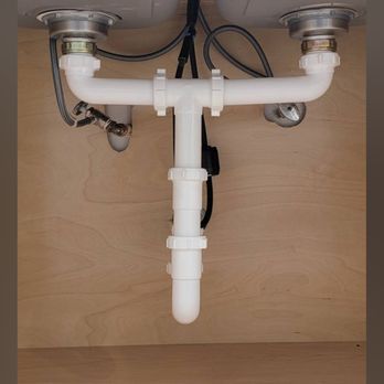 White plumbing pipes under a sink, connected to two drain openings and a vertical drainpipe.