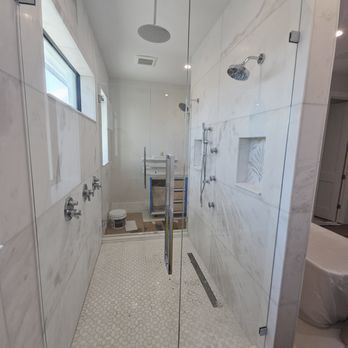 Spacious, modern bathroom with white marble walls and floor, glass shower doors, and multiple showerheads.