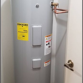 A GE electric water heater in a closet, with a yellow energy guide sticker. Copper pipes are connected at the top.