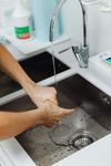 Person washing hands in a stainless steel sink under running water in a medical or clinical setting.