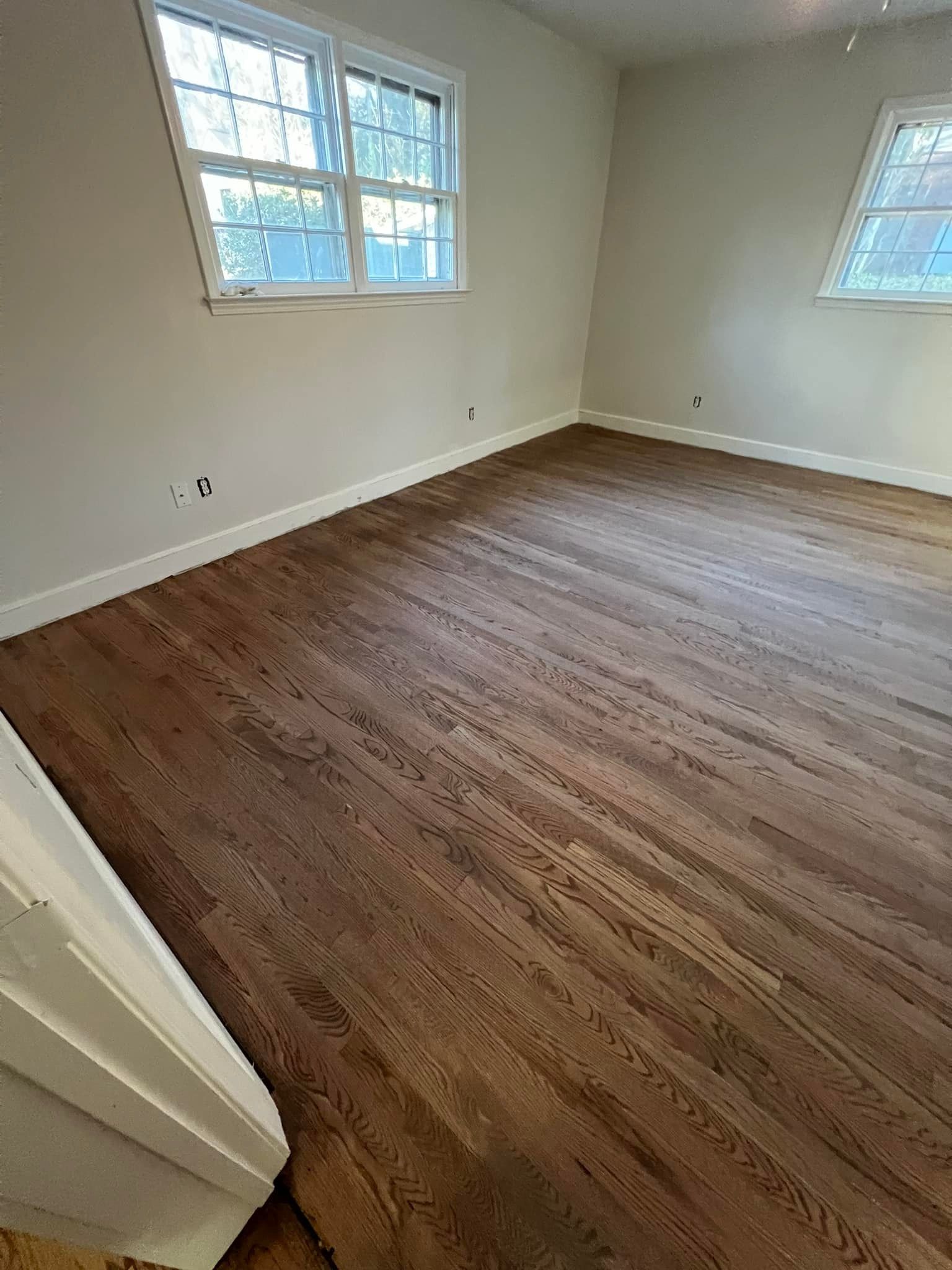 An empty room with hardwood floors and two windows.