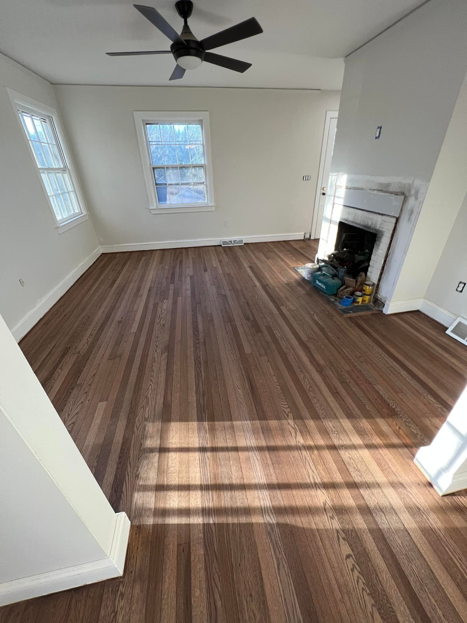 A living room with hardwood floors , a fireplace and a ceiling fan.