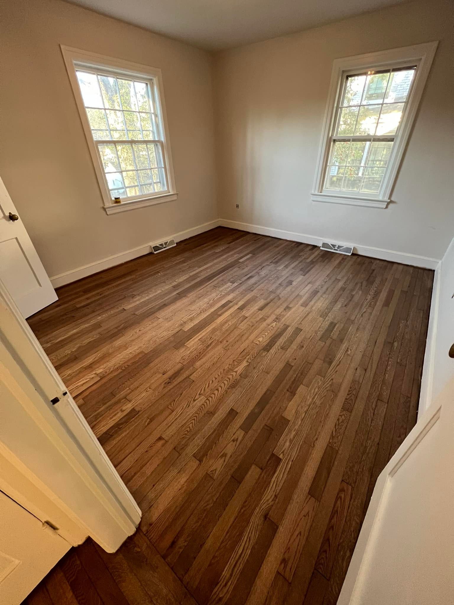 An empty room with hardwood floors and two windows.