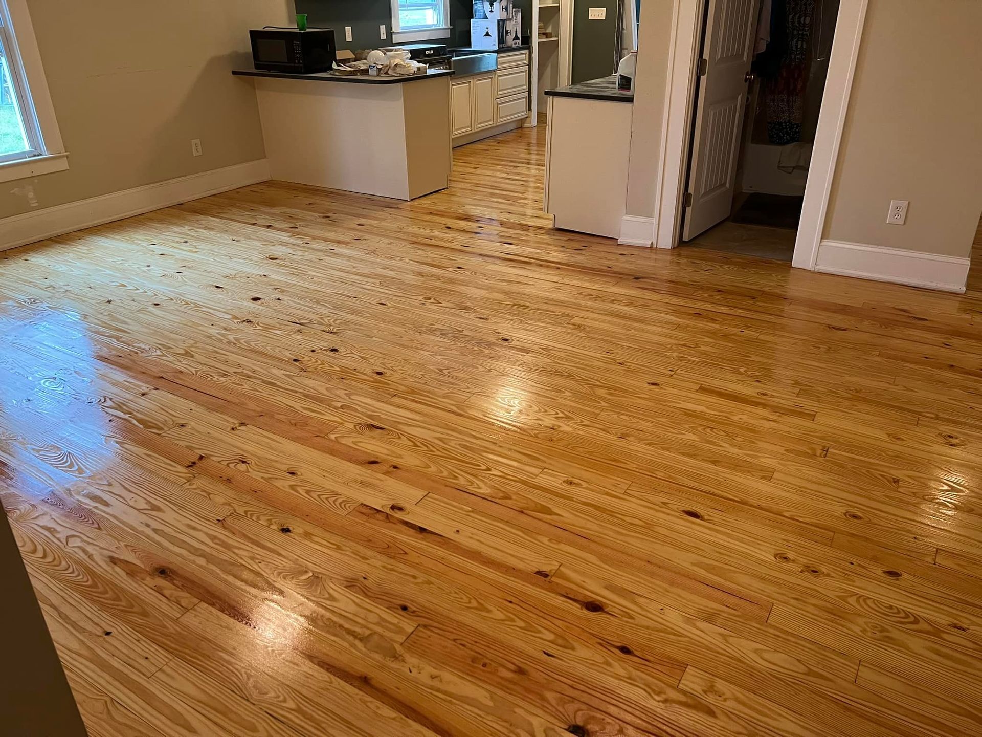 A living room with hardwood floors and a kitchen in the background.