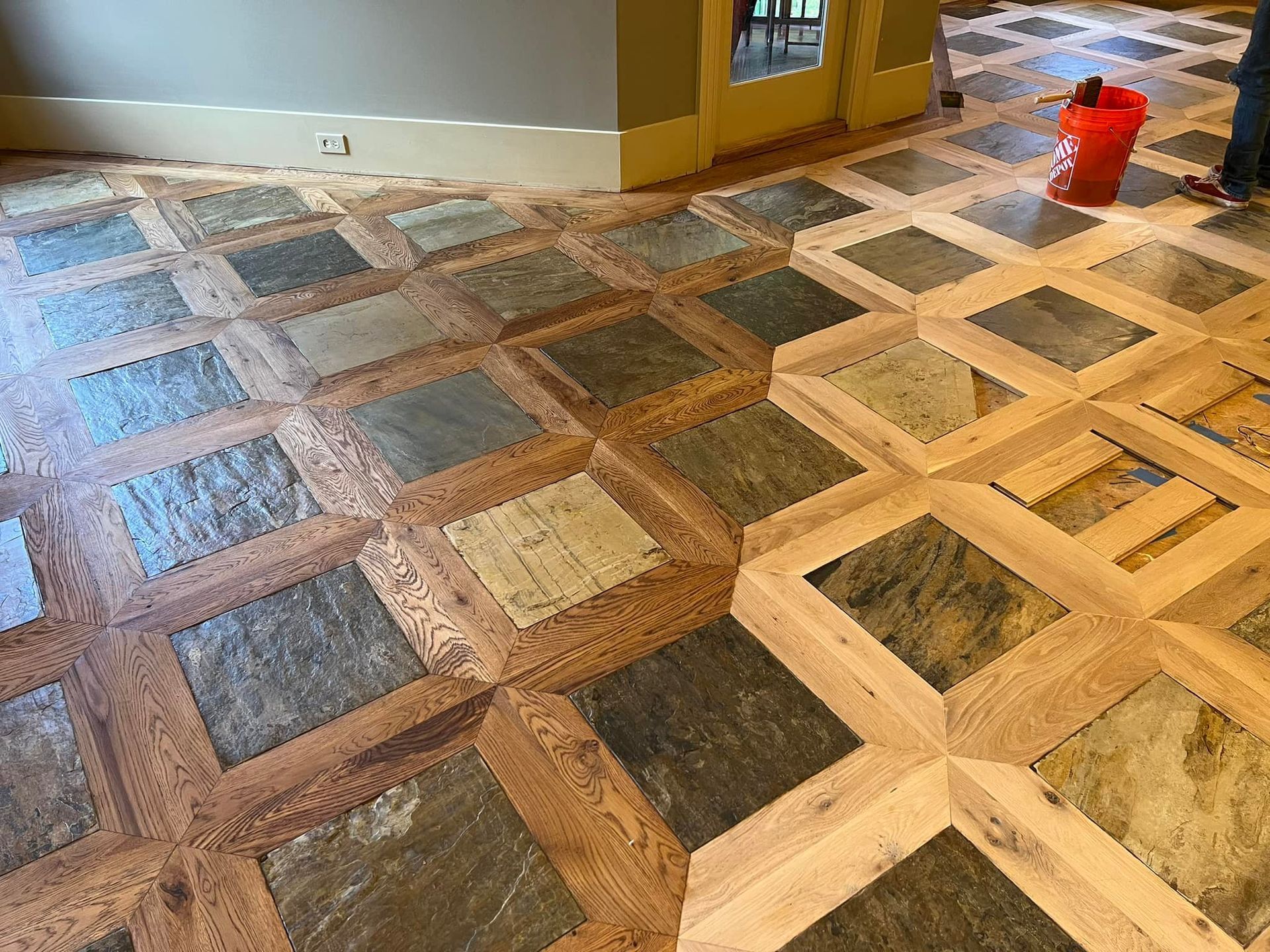A person is cleaning a wooden floor with a red bucket.