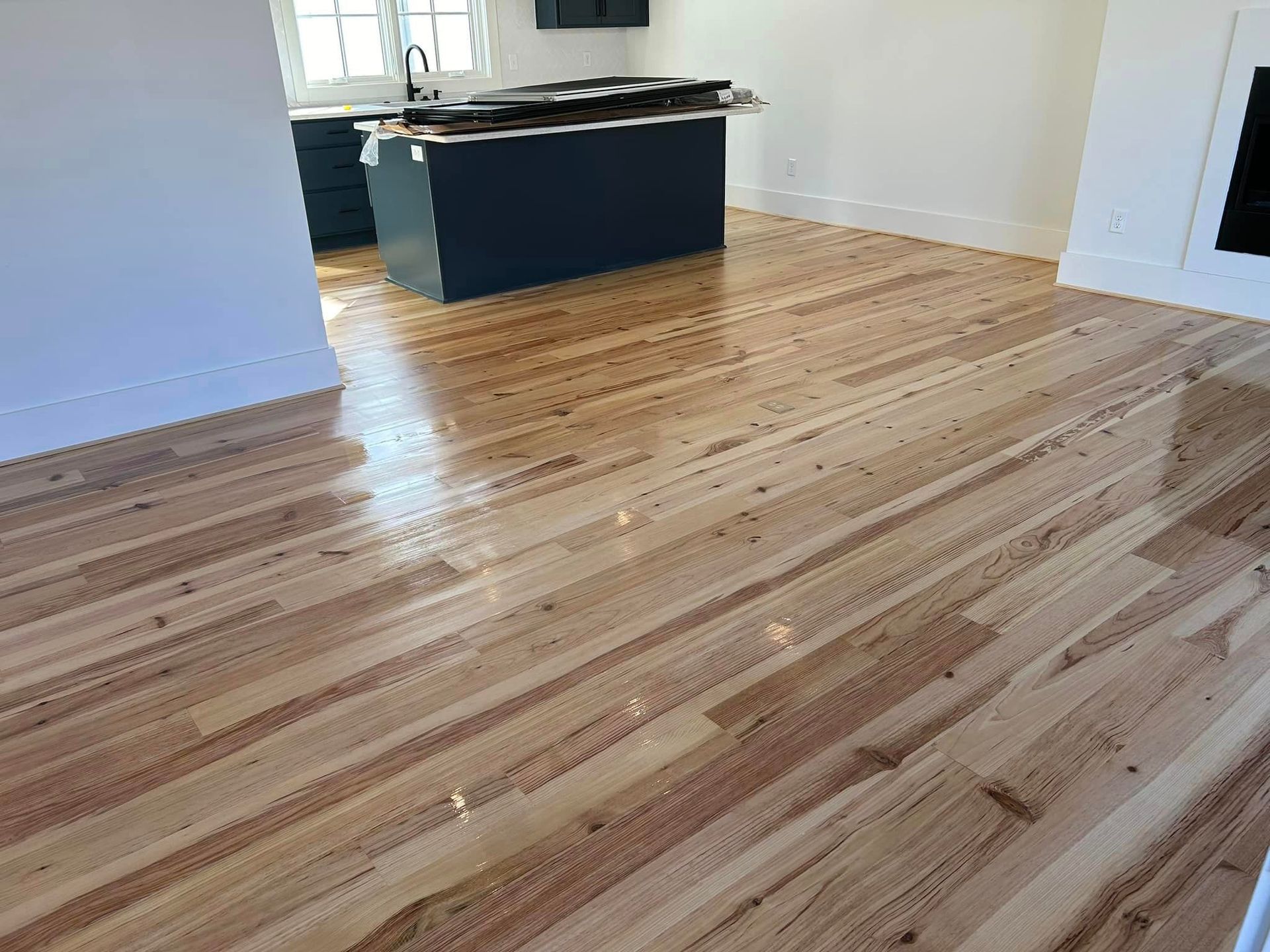 A living room with a wooden floor and a kitchen in the background.