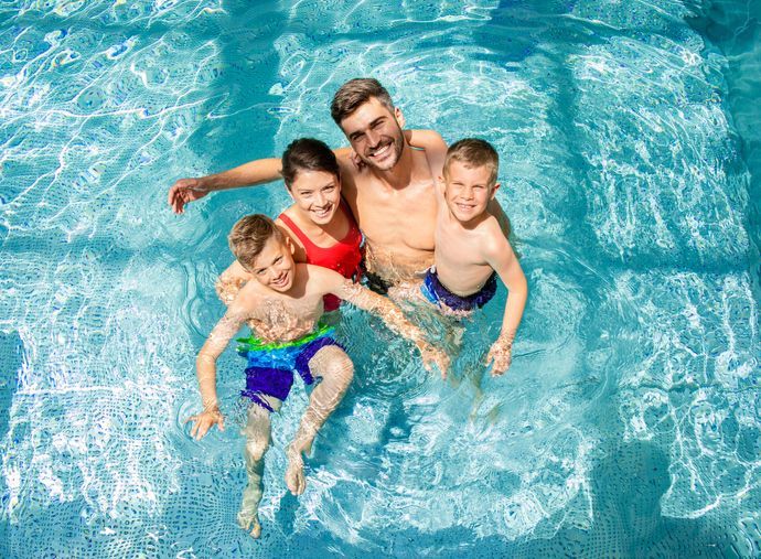 Top view of smiling family of four having fun and relaxing in indoor swimming pool at hotel resort