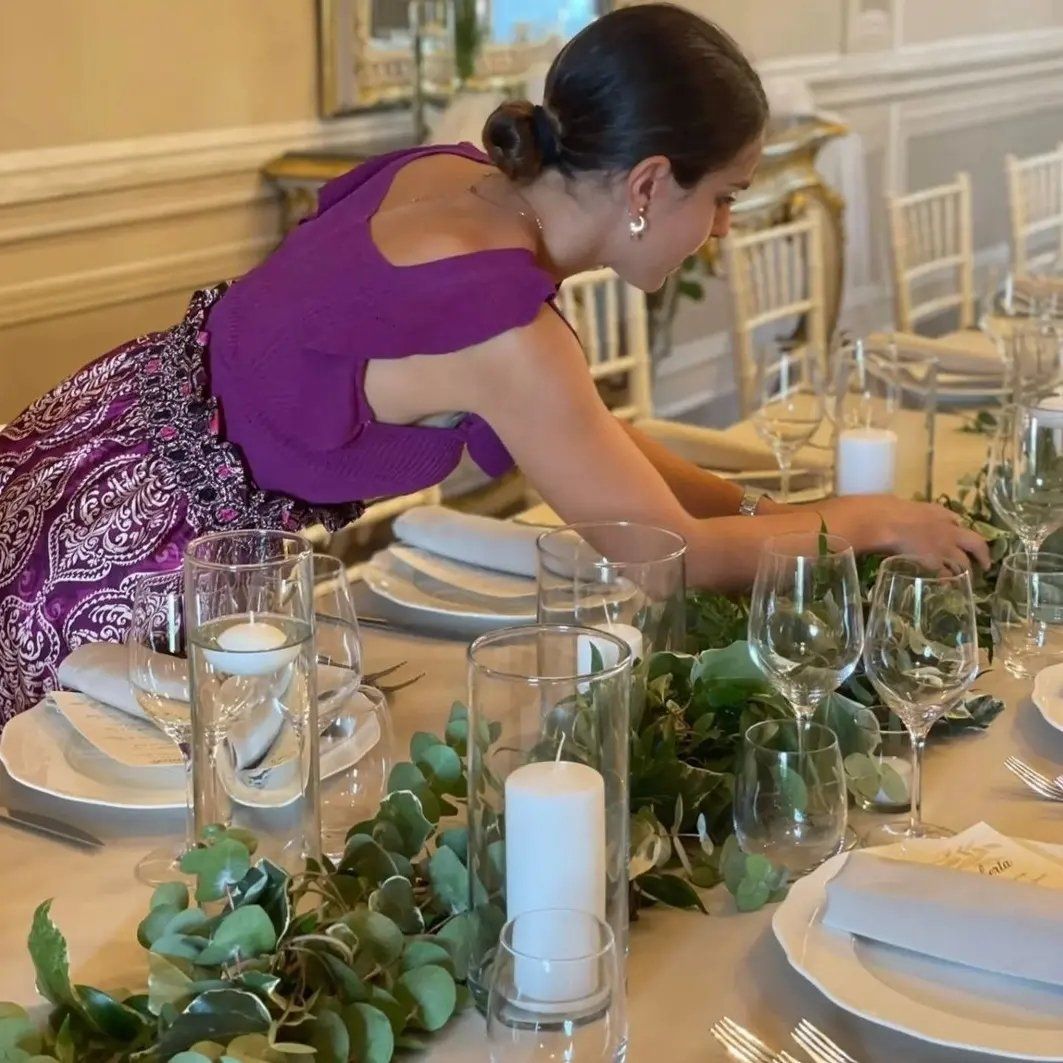 Una donna con un vestito viola è seduta a un tavolo con piatti, bicchieri e candele.