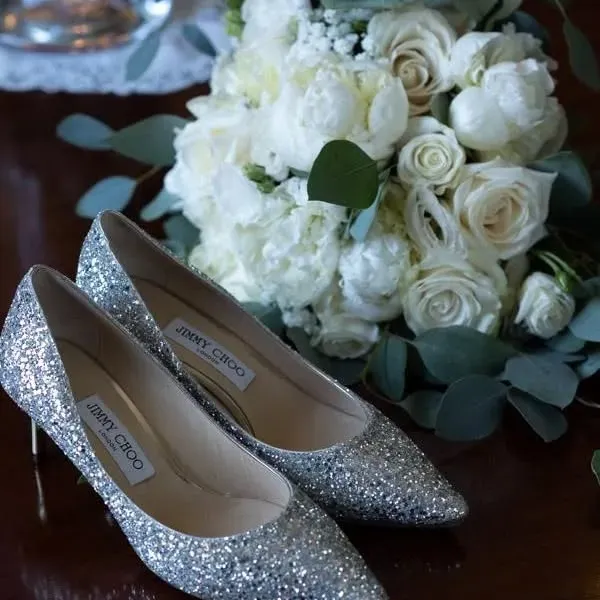 Un paio di scarpe Jimmy Choo accanto a un bouquet di rose bianche