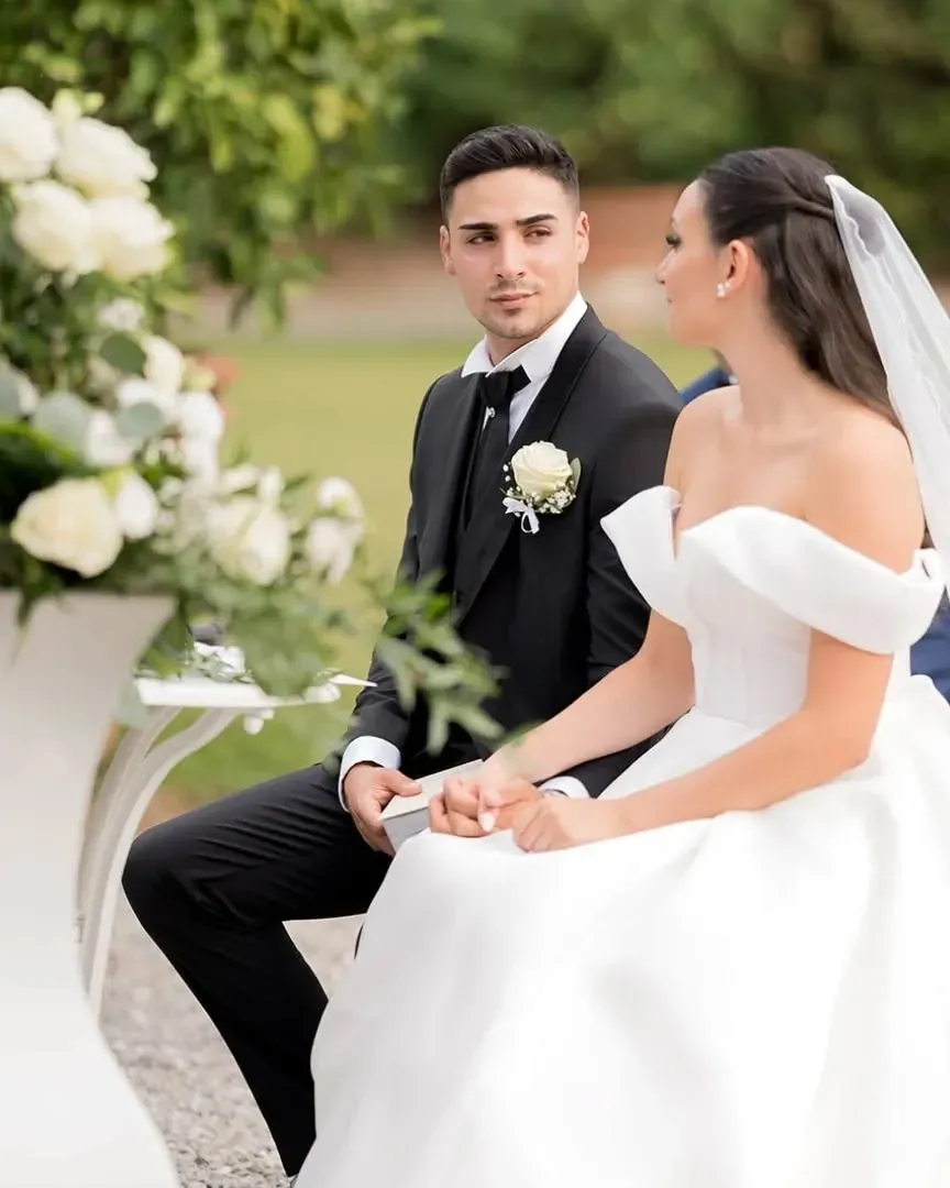 Una sposa e uno sposo sono seduti su una panchina e si tengono per mano.