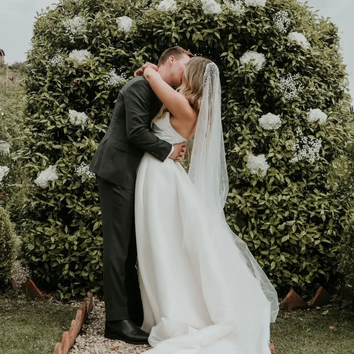 Una sposa e uno sposo che si baciano davanti a un cespuglio di fiori bianchi