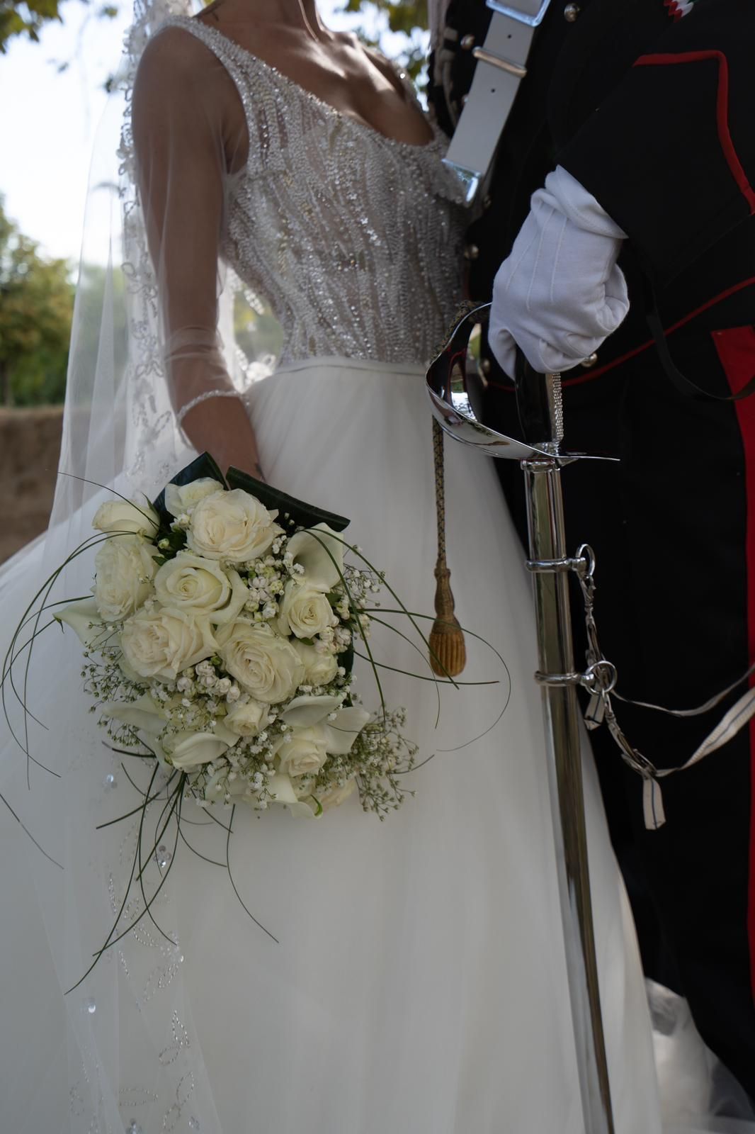 Una sposa tiene in mano un mazzo di rose bianche mentre è in piedi accanto a un uomo in uniforme militare.