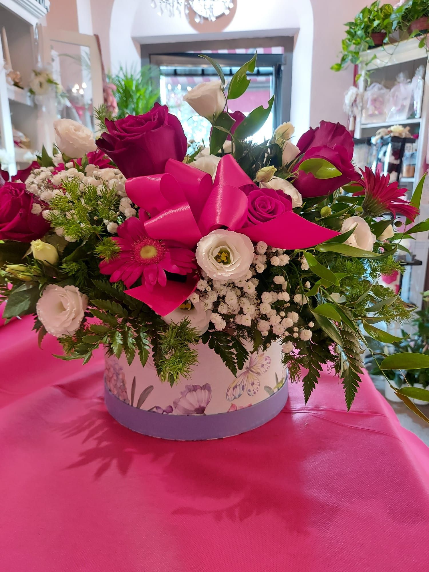 Una scatola piena di fiori è appoggiata su un tavolo rosa.