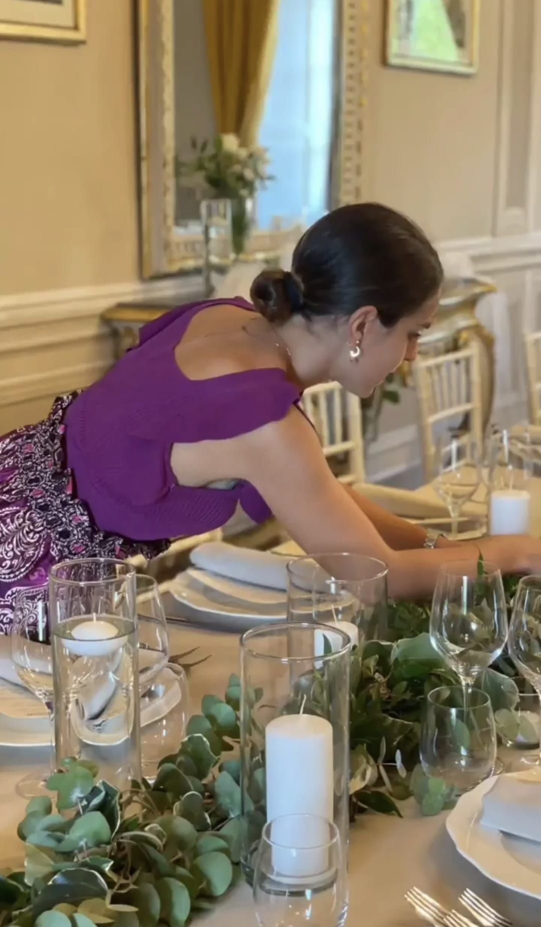 Una donna con un vestito viola sta apparecchiando la tavola per un ricevimento di nozze.