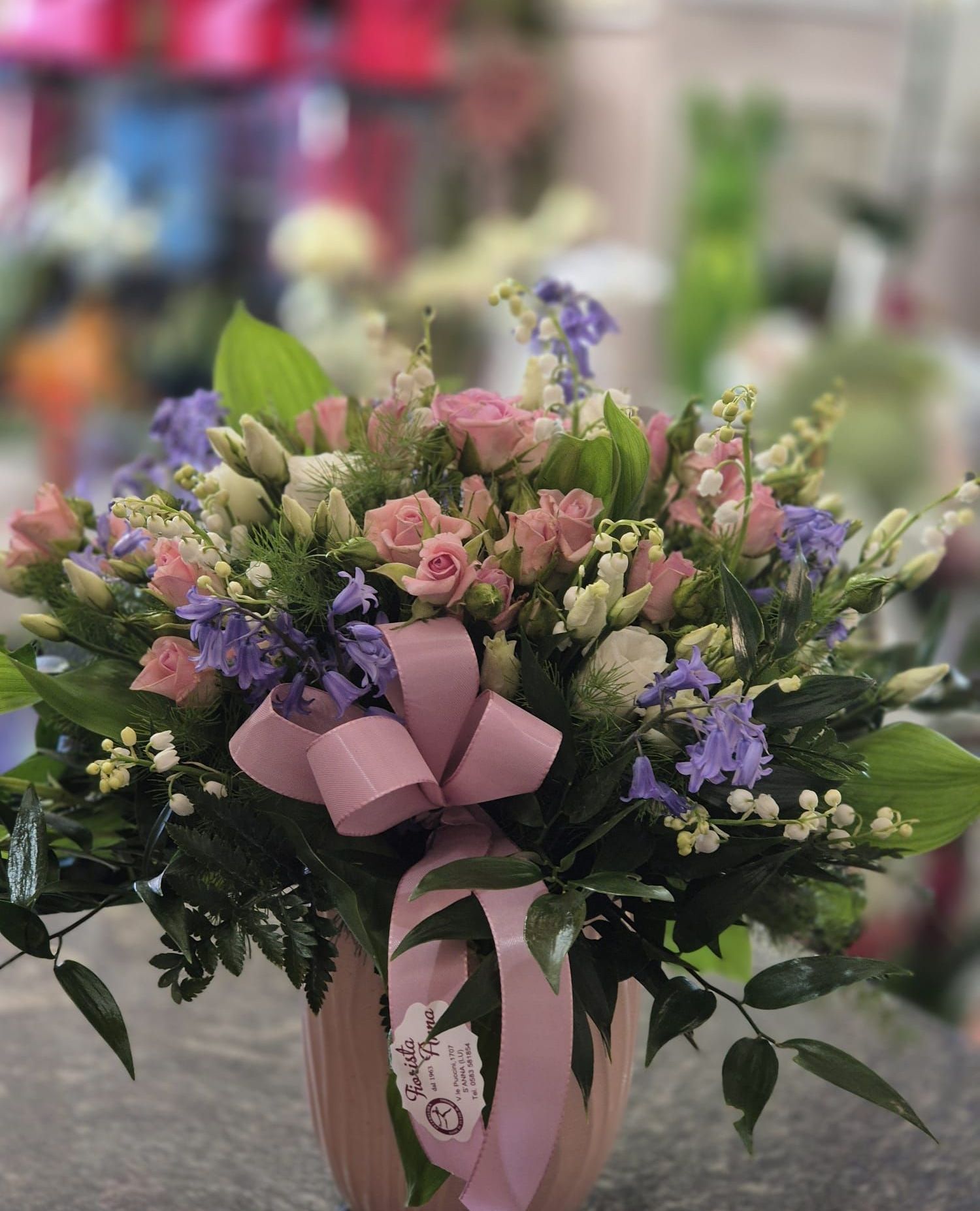Un vaso pieno di fiori rosa e viola con un fiocco rosa.