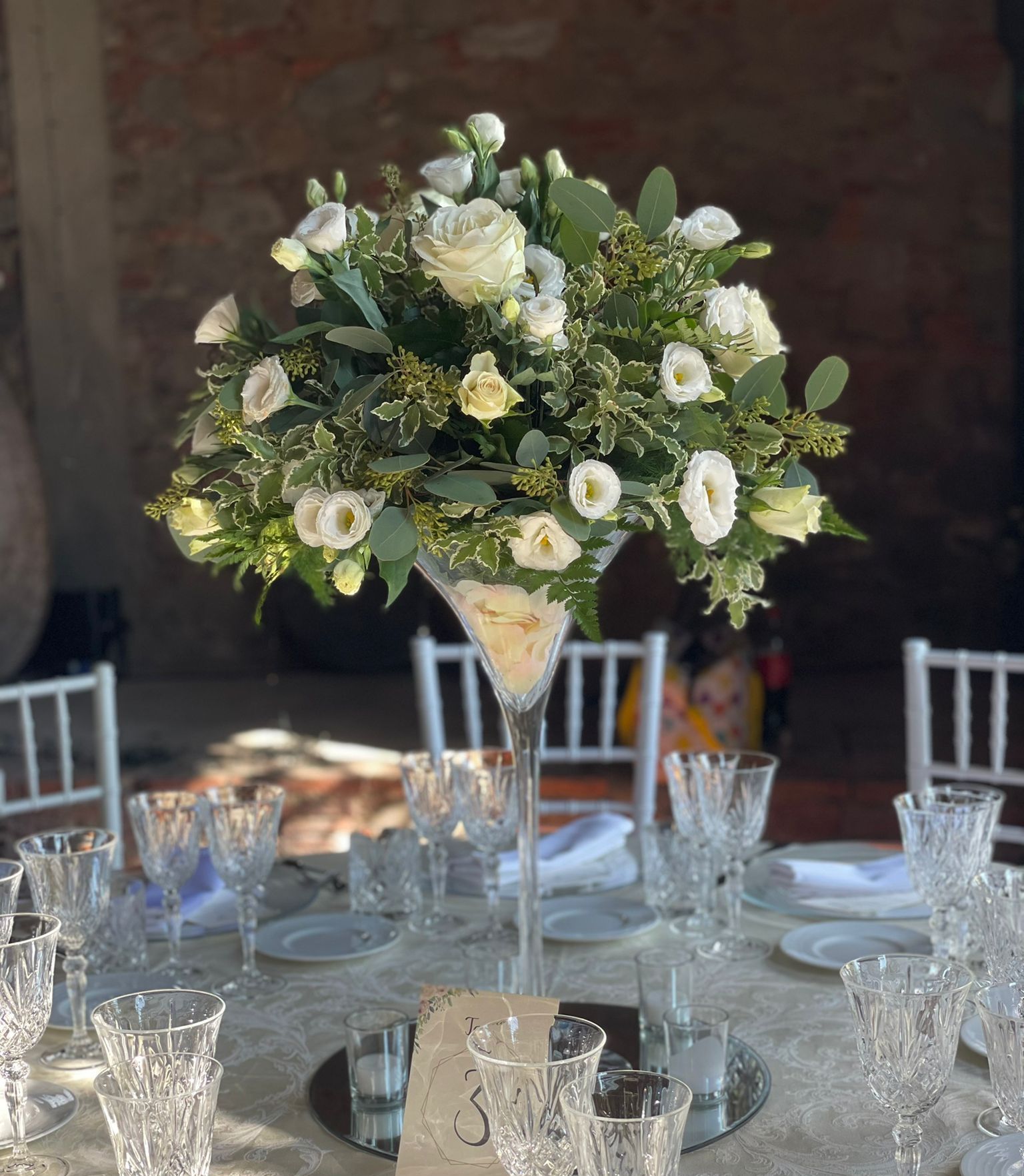 Un bicchiere da martini pieno di fiori bianchi è appoggiato su un tavolo.