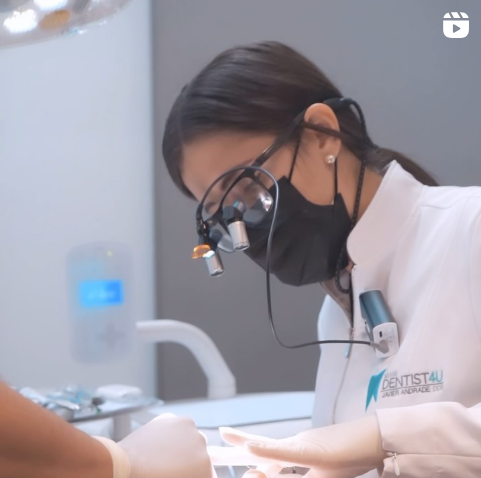A dentist wearing a mask and glasses is working on a patient