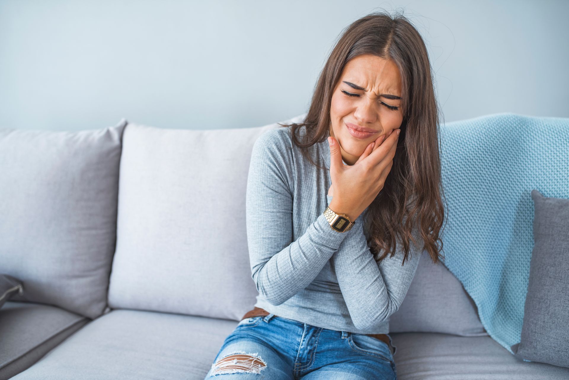 A woman is sitting on a couch with a toothache.