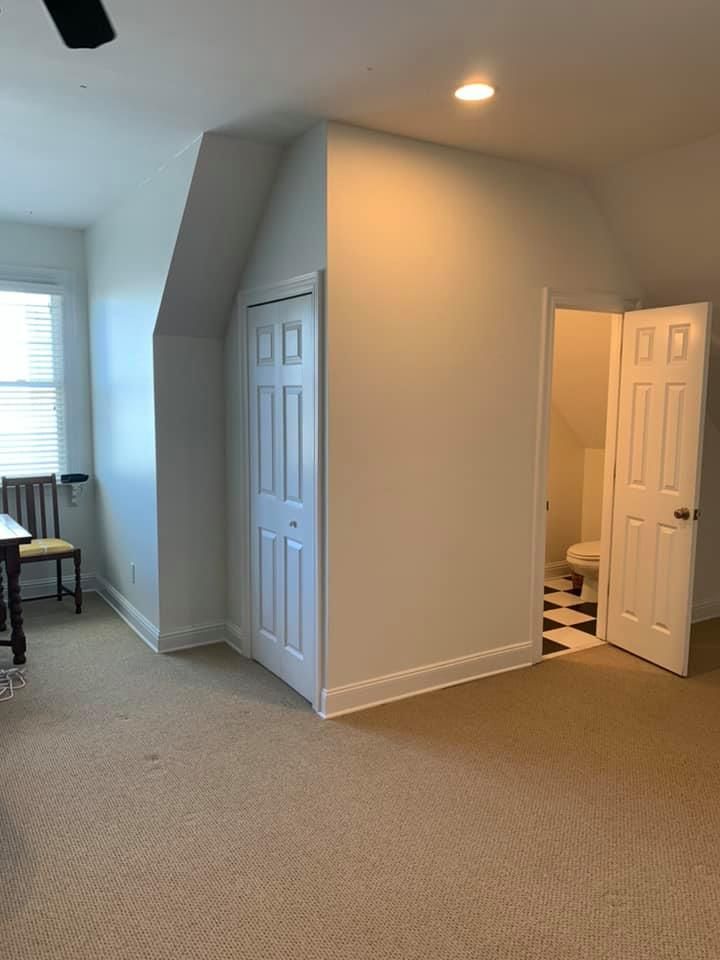 Bedroom with beige carpet, slanted wall, closet, open bathroom door.