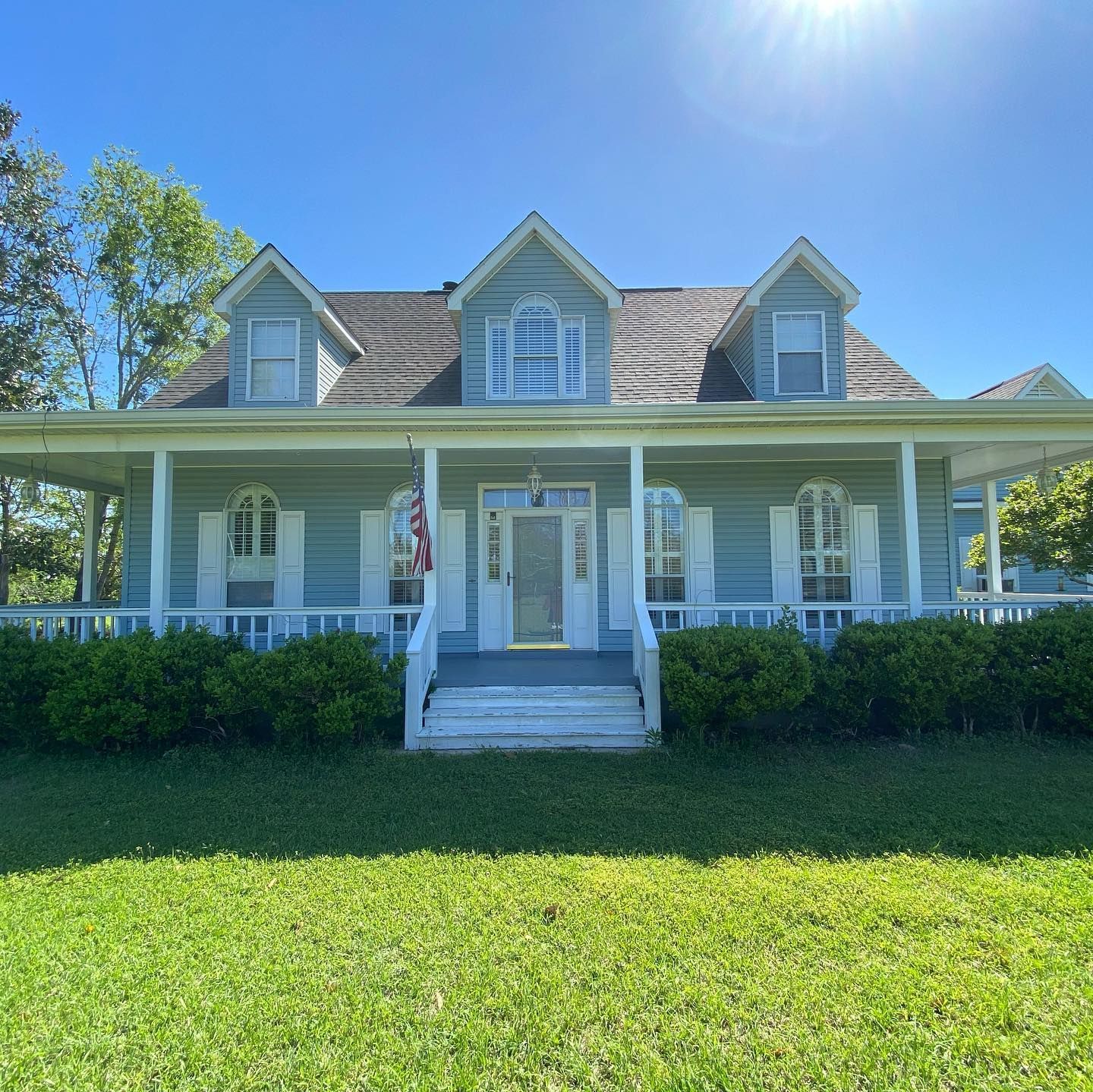 Light blue house with white trim, front porch, and green lawn under a bright blue sky.